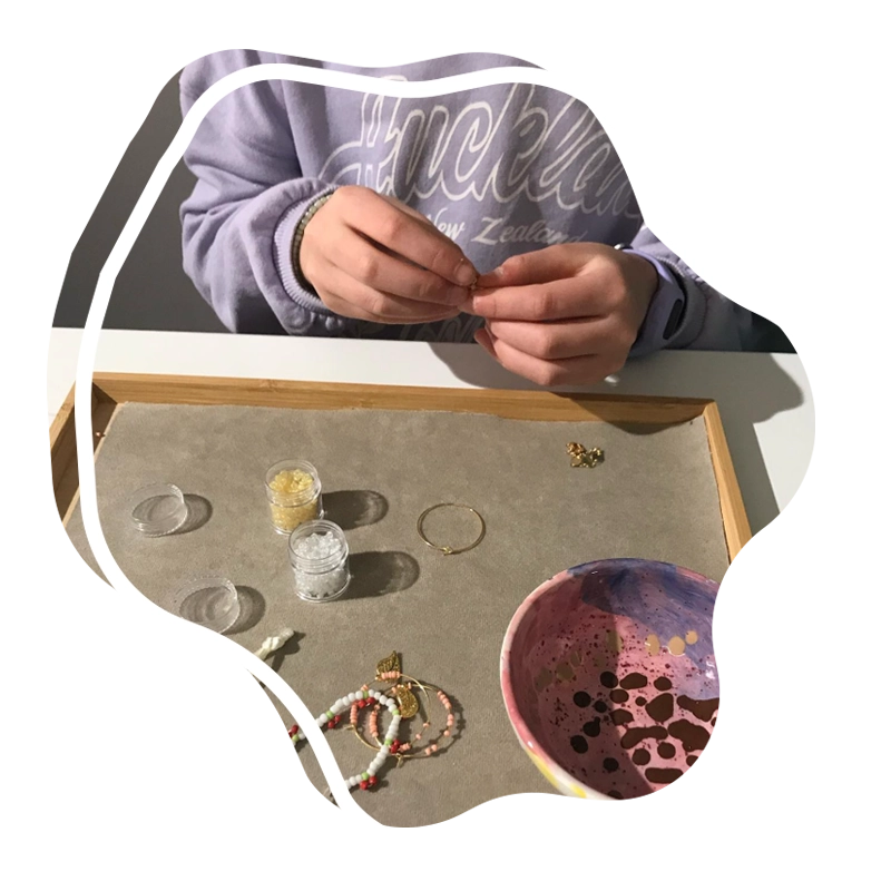 pige sidder foran en bakke med perler på og er i gang med at lave et perlearmbånd